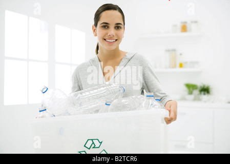 Teen girl transportant des bacs de recyclage plein de bouteilles en plastique, smiling at camera Banque D'Images