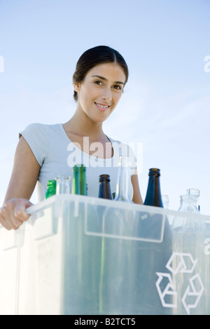 Femme transportant corbeille remplie de bouteilles en verre, smiling at camera Banque D'Images
