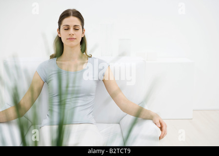 Femme assise dans un fauteuil, les yeux clos, les plantes en premier plan Banque D'Images