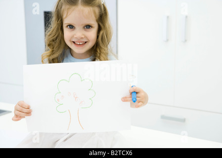 Little girl holding dessin d'arbre, smiling at camera Banque D'Images