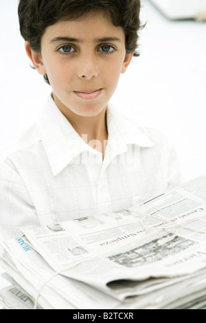 Boy carrying pile de journaux, smiling at camera Banque D'Images