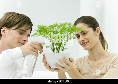 Woman holding potted plant, l'homme à l'aide de spray bottle Banque D'Images