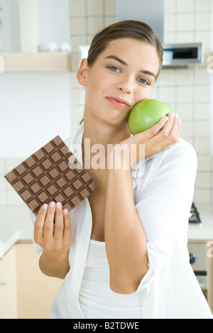 Femme tenant une grande barre de chocolat dans une main, dans l'autre apple, smiling at camera Banque D'Images