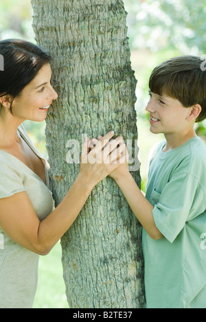 Mère et fils embrassant arbre, smiling at each other Banque D'Images