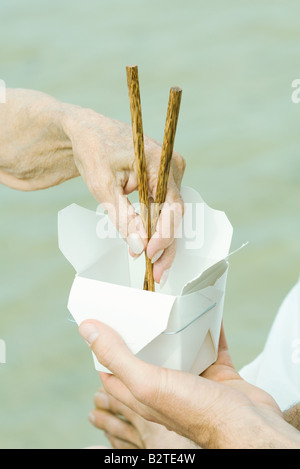 Homme main tenant le contenant, senior woman's hand reaching dans avec des baguettes, cropped Banque D'Images