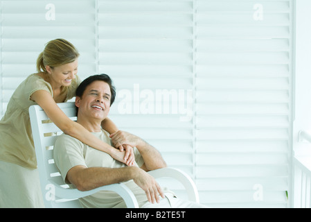 Homme assis dans une chaise, femme debout derrière, enlacés, smiling Banque D'Images