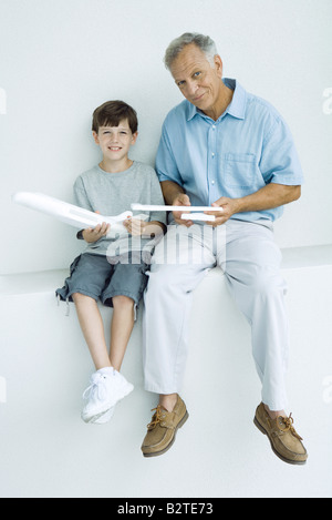 Grand-père et petit-fils assis côte à côte, holding model airplane pièces, smiling at camera Banque D'Images