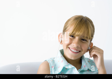 Girl listening to earphones, smiling at camera Banque D'Images