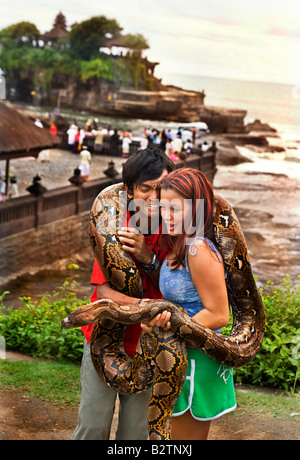 Un couple de touristes indonésiens posent pour des photos tenant un grand python par Tanah Lot un ancien temple hindou par la mer à Bali Banque D'Images