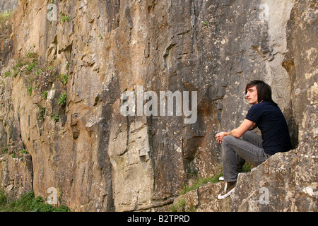 Jeune homme assis par rock face Banque D'Images