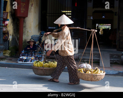 Femme chapeau conique en bananes panier épaule marche Hoi An Vietnam Banque D'Images