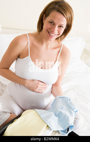 Femme enceinte vêtements bébé emballage dans suitcase smiling Banque D'Images