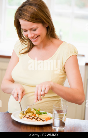 Femme enceinte dans la cuisine manger du poulet et légumes smiling Banque D'Images