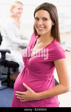 Femme enceinte au travail holding belly smiling avec un collègue en arrière-plan Banque D'Images