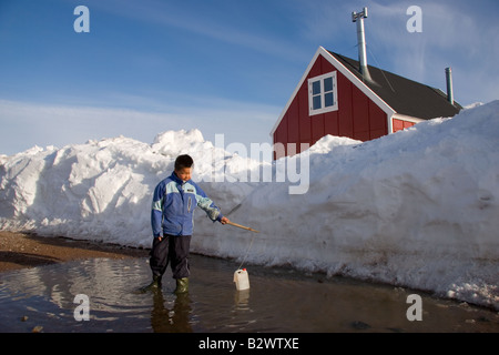Un jeune garçon Inuit joue avec un carton vide dans une flaque d'eau dans le village d'Ittoqqortoormiit Scoresbysund,, dans l'Est du Groenland Banque D'Images