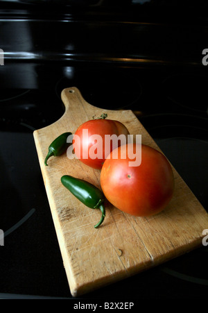 Deux tomates et piments jalapeño deux sur une planche à découper en bois. Banque D'Images