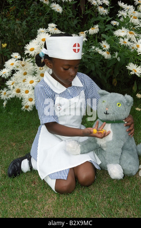 Petite fille noire dans un uniforme d'infirmière donnant son jouet cat une injection. Banque D'Images