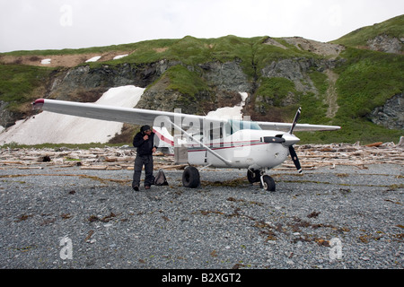 L'inspection de pilote avant de prendre son avion de d'une plage couverte de bois flottant dans Katmai, Alaska Banque D'Images