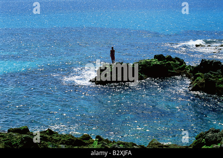 Femme à l'extérieur debout sur de grosses roches Oceanside (loin/silhouette) Banque D'Images