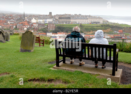 Deux vieillards assis sur un banc à la recherche à Whitby Harbour sur un jour étés gris Yorkshire Angleterre UK Banque D'Images