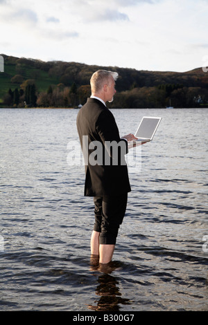 Businessman with laptop computer debout dans le lac Windermere, Cumbria, Angleterre Banque D'Images