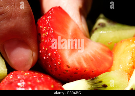 Les doigts de la prise d'une fraise rouge de fruits fraîchement coupé Banque D'Images