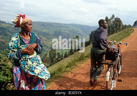 Femme en vêtements traditionnels et man pushing bicycle uphill sur chemin de terre, l'Ouganda, l'Afrique Banque D'Images