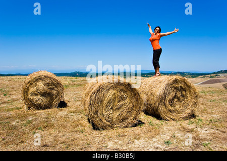 Femme d'âge moyen qui représente la liberté en se tenant debout sur les rouleaux de foin dans le champ agricole au cours de l'heure d'été en Toscane Italie Banque D'Images