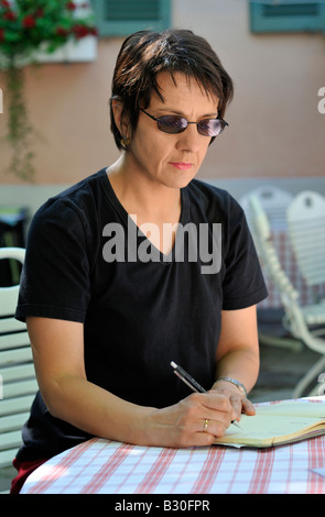 Femme assise à une table et d'écrire dans un livre Banque D'Images