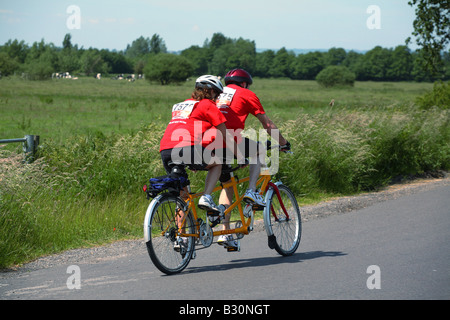 La charité des cyclistes sur un tandem jaune. Banque D'Images