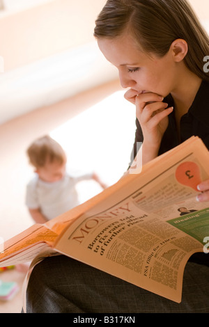 Mère regardant nouvelles financières inquiétantes dans le papier à l'enfant dans l'arrière-plan Banque D'Images