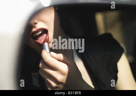 Reflet de young woman applying lipstick dans le rétroviseur Banque D'Images