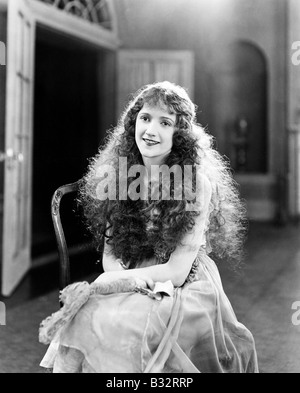 Jeune femme avec de longues boucles, cheveux bouclés, frisés assis sur une chaise et souriant Banque D'Images