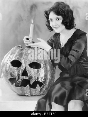 Jeune femme tenant une bougie allumée sur un Jack O' Lantern and smiling Banque D'Images