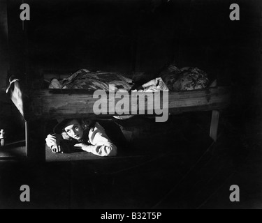 Jeune femme se cachant sous le lit Banque D'Images