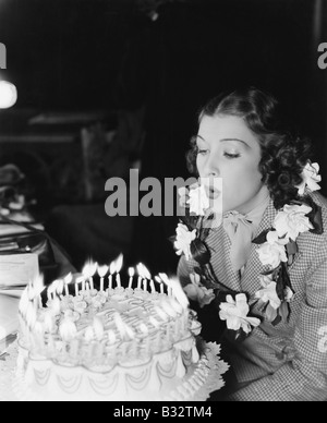 Profil d'une jeune femme soufflant au large de bougies sur un gâteau d'anniversaire Banque D'Images