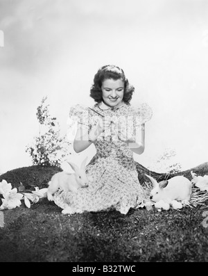 Jeune femme assise sur l'herbe avec des lapins en peinture d'un œuf de Pâques Banque D'Images