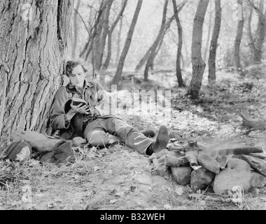 L'homme assis à côté d'un feu dans les bois et la lecture d'un livre Banque D'Images