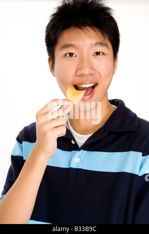 Un jeune homme asiatique eating potato chips Banque D'Images