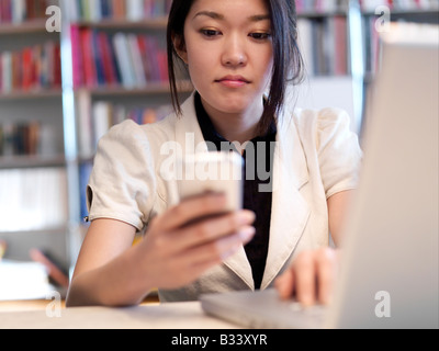 Une jeune asiatique s'assoit à son bureau travaillant sur son ordinateur portable. Banque D'Images