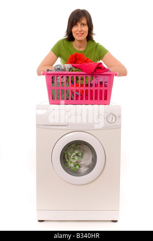 Jeune femme caucasienne souriante portant un t-shirt vert appuyé sur un panier à linge rose rempli de vêtements qui est sur un lave-linge Banque D'Images