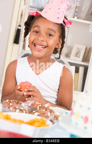 Jeune fille de party assis à table avec un petit gâteau smiling Banque D'Images