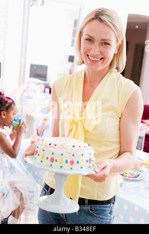 Woman at party holding birthday cake smiling Banque D'Images