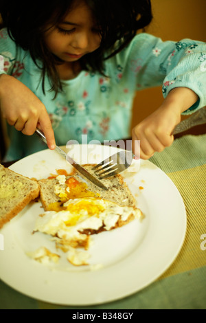 Apprendre à utiliser un couteau et fourchette une fille de cinq ans mange œuf frit sur toast Banque D'Images