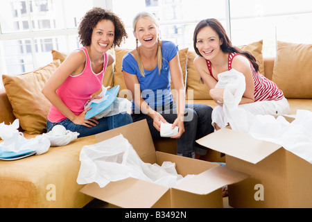 Trois girl friends unpacking boxes in new home smiling Banque D'Images
