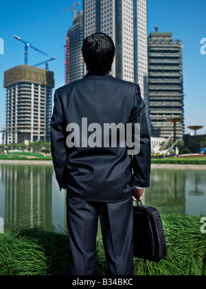 Homme d'affaires chinois ressemble à la construction et la construction de plusieurs gratte-ciel à travers l'étang. Banque D'Images