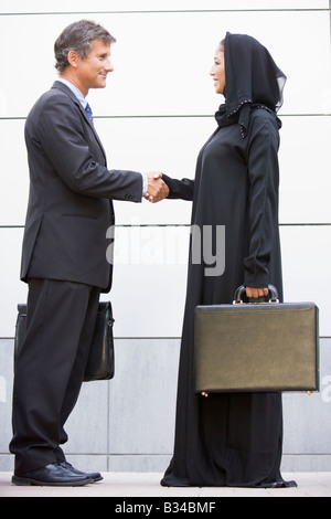 Deux businesspeople standing en plein air avec porte-documents shaking hands and smiling Banque D'Images