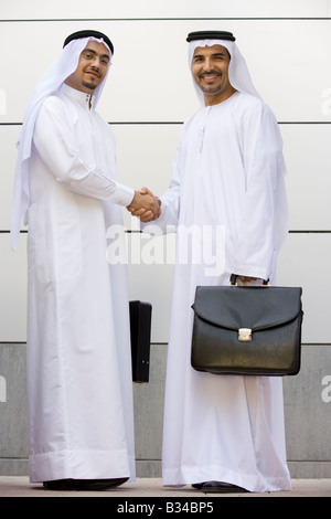 Deux businessmen standing en plein air avec porte-documents shaking hands and smiling Banque D'Images
