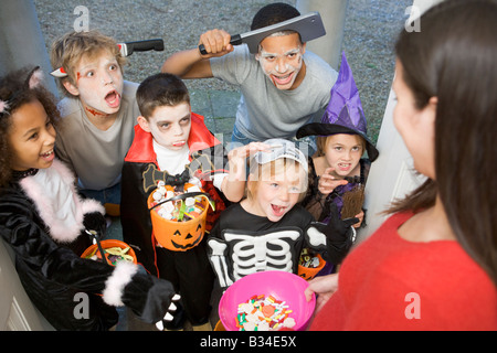 Six enfants en costumes trick or treating at woman's house Banque D'Images