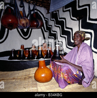 L'Ouganda, le sud de l'Ouganda, Mbarara. Une femme Bahima avec son lait en bois pots (connu comme ekyanzi) et les gourdes, qui sont conservés sur un relevé spécial étape dans un coin du salon. Les maisons sont souvent décorées de motifs africains originaux.Les Bahima Banyarwanda sont des personnes anglophones vivent près de la frontière du Rwanda, dans le sud de l'Ouganda. Elles maintiennent de longues cornes bovins Ankole, un Africain de race taurine avec des origines remontant à avant l'introduction de ou le champ de courses de zébus dans la Corne de l'Afrique au cours de l'invasion venant de l'Arabie au septième siècle avant Jésus-Christ. Banque D'Images